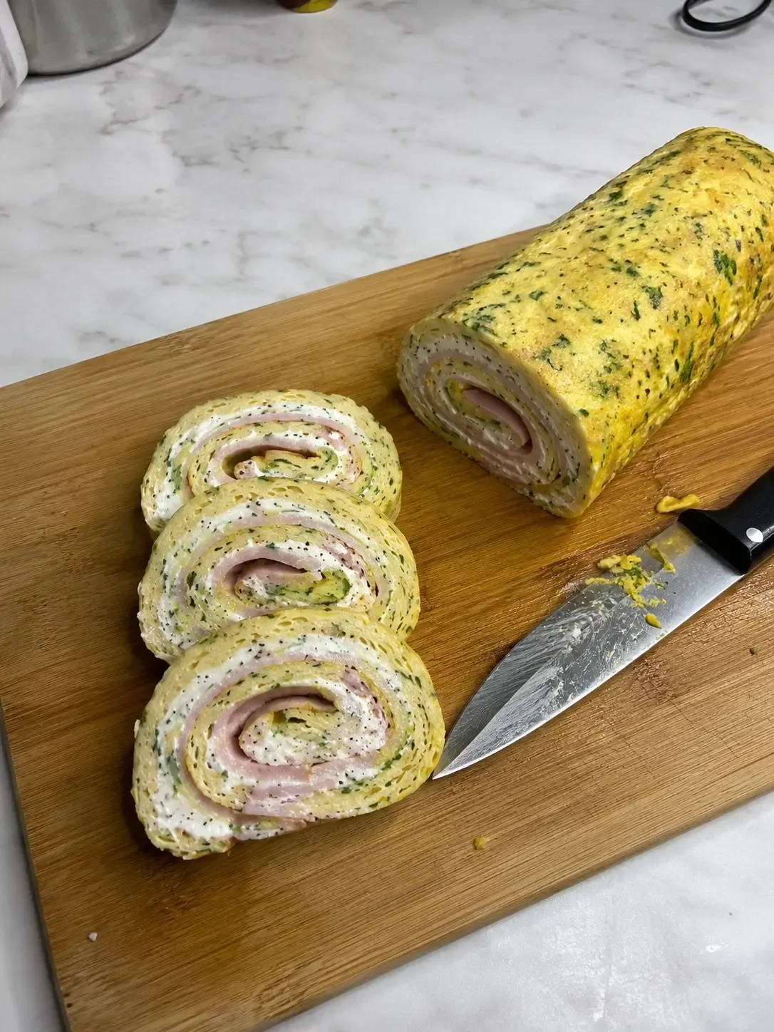 Rolada Keto Tortilla z jajek z serkiem smietankowym szynką i ogórkiem na desce do krojenia
