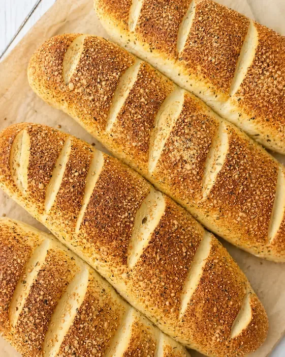 Miękkie domowe bagietki w stylu Subway posypane parmezanem i ziołami, ułożone na papierze do pieczenia